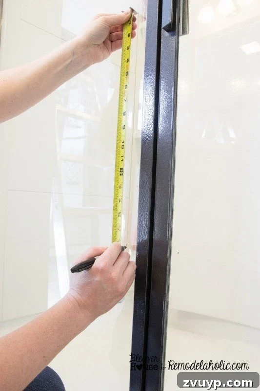 Marking the glass shower door for horizontal moulding placement, ensuring even pane sizes.