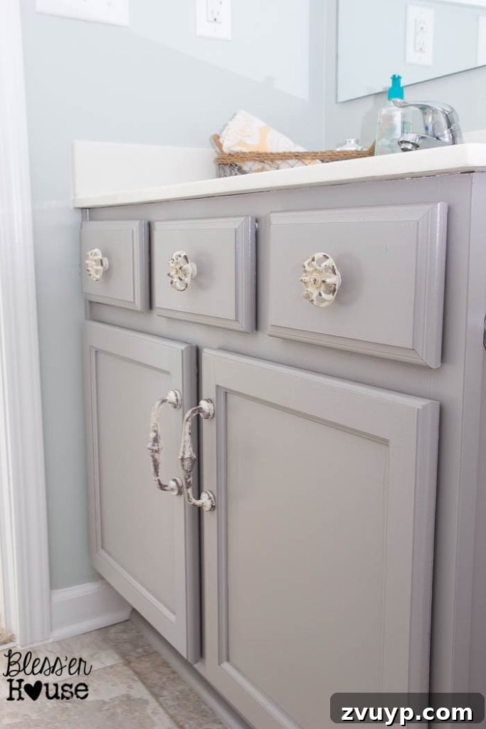 Effortless Cabinet Transformation for Beginners 14 A beautifully updated bathroom vanity with light grey painted cabinets and new hardware, despite challenging lighting.