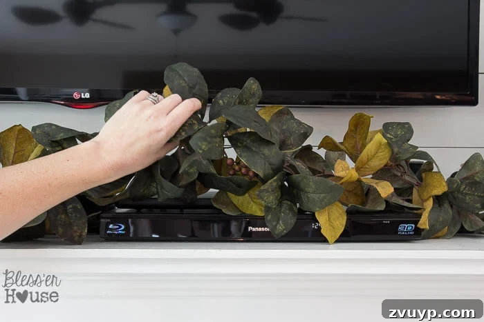 Elevate Your Mantel: Smart Ways to Conceal Electronics 5 Magnolia garland strategically placed on a mantel to hide electronic devices like a PlayStation, while allowing remote signals to pass through.