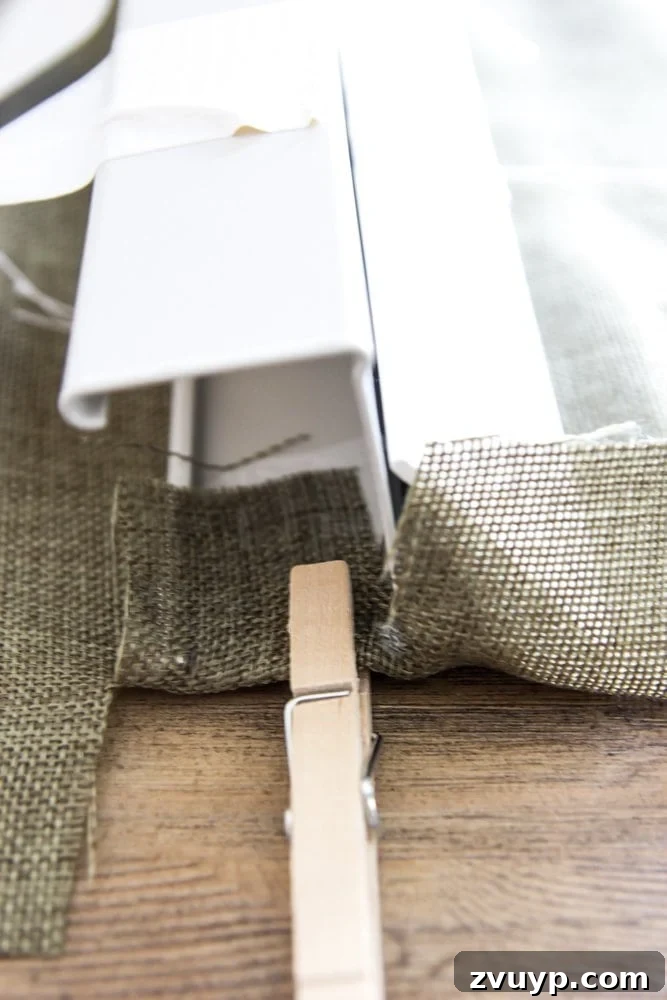 Burlap Roman Shades A Clever Blind Transformation 11 Fabric tab being hot-glued inside the blind header and secured with a clothespin, detailing the attachment method for the top of a DIY Roman shade.