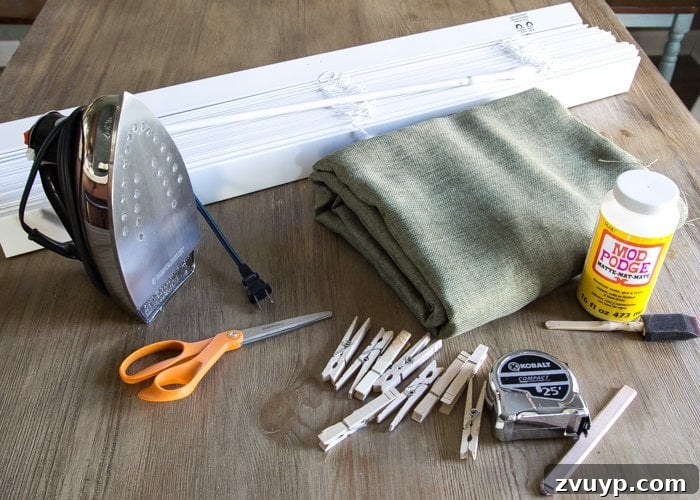 Burlap Roman Shades A Clever Blind Transformation 3 Detailed shot of DIY Roman shade supplies including green burlap fabric, hot glue gun, scissors, tape measure, and clothespins, laid out neatly on a wooden surface.
