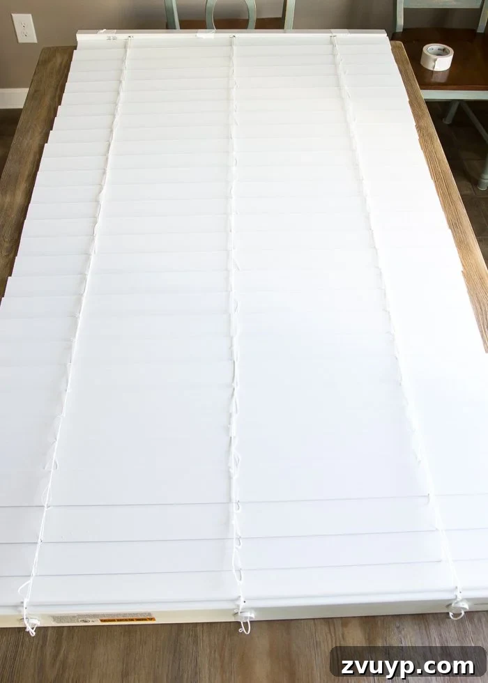 Burlap Roman Shades A Clever Blind Transformation 4 Detailed view of cordless blinds laid face down on a work table, secured with duct tape to prevent retraction during the DIY Roman shade conversion process.