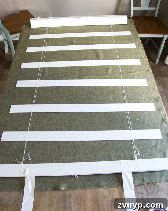 Burlap Roman Shades A Clever Blind Transformation 8 Fabric laid beneath a partially disassembled blind, with slats being spaced evenly. Highlights the importance of accurate measurement and full blind extension to prevent errors in Roman shade creation.