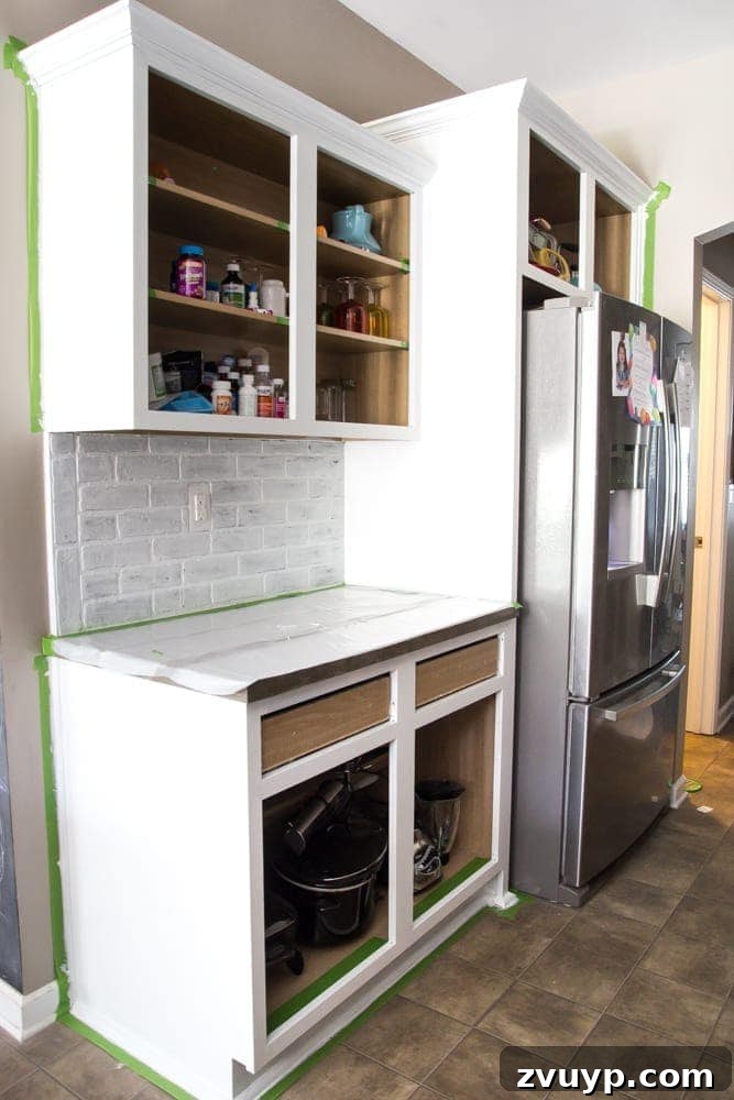 Flawless Cabinets: Paint Your Kitchen Like a Seasoned Pro 11 Painting kitchen cabinet frames with a roller and brush, protected by painter's tape and drop cloths. DIY cabinet painting process.