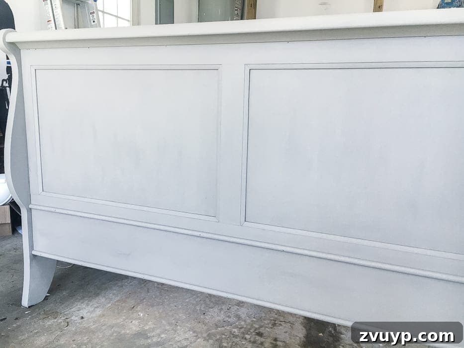 From Weathered to Wonderful A Painted Bed Revival 4 Applying the French Linen base coat to the sleigh bed, showing the initial transformation from dark cherry to light beige.