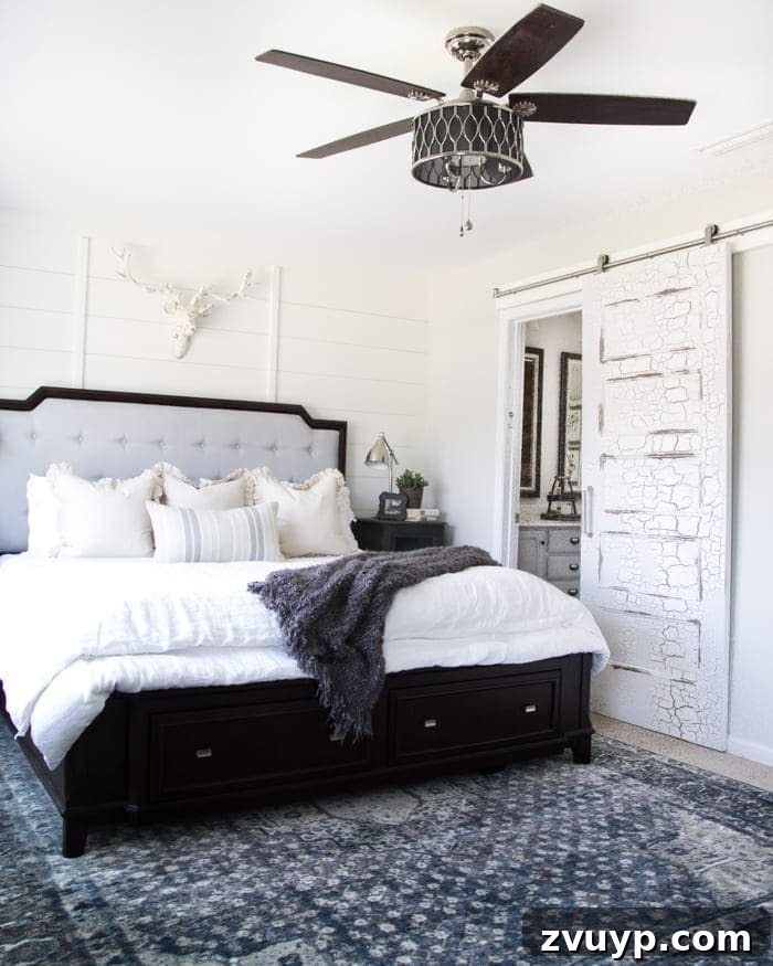 Transform Your Builder Home with Farmhouse Style 6 A farmhouse master bedroom featuring a distressed white sliding barn door on a black track, connecting to a bathroom and saving space.