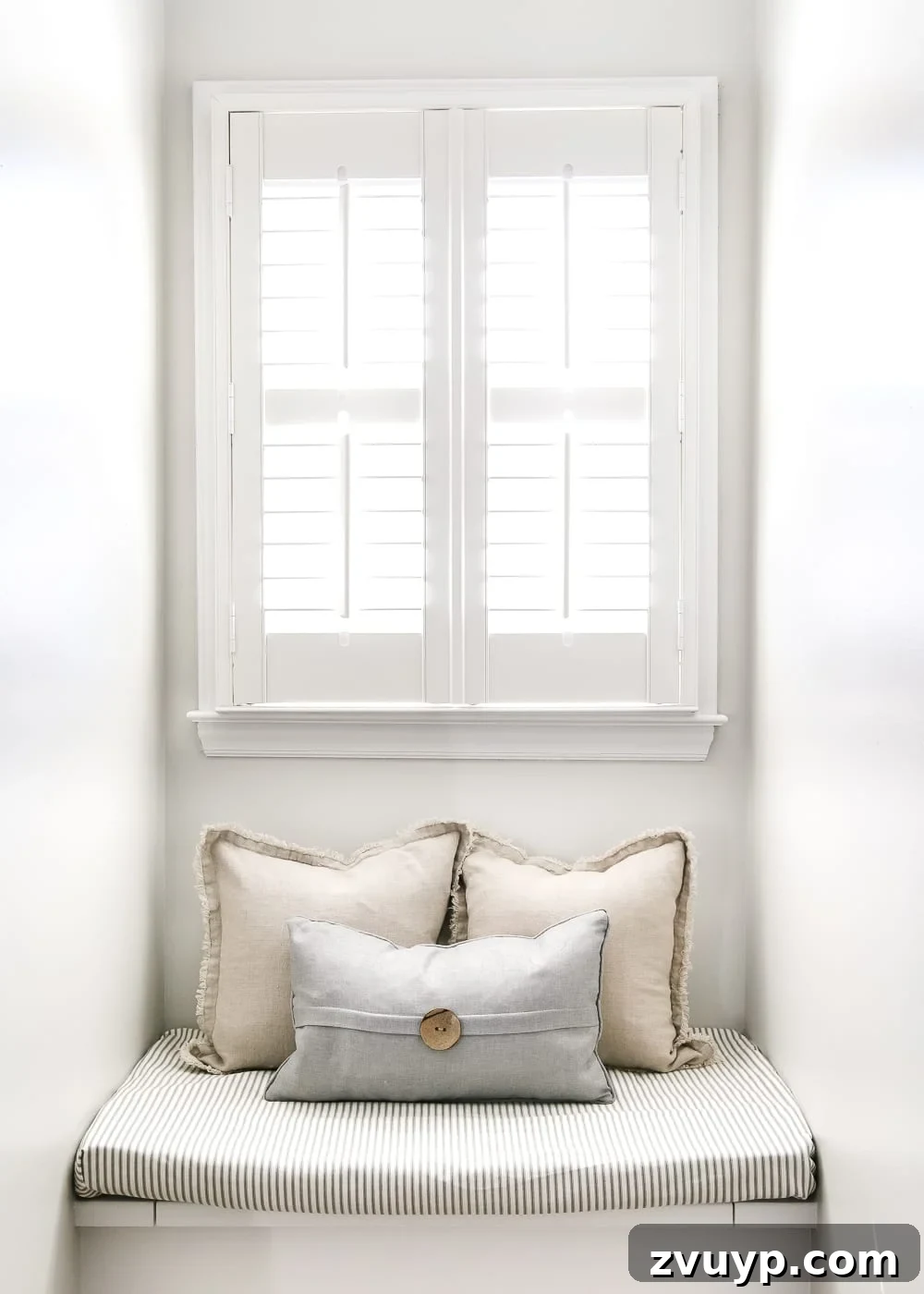 The inviting window seat with a ticking stripe cushion and decorative pillows, offering storage below.