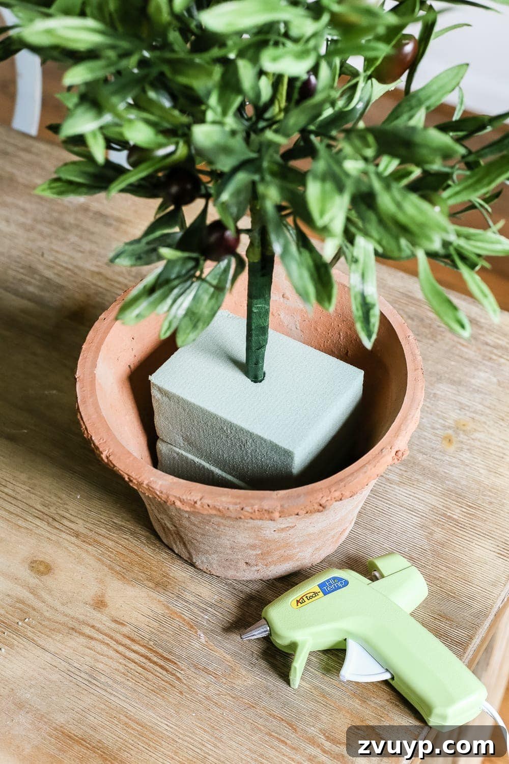 Craft Your Own Olive Topiary 7 Inserting bundled faux olive stems into stacked dry floral foam blocks in a pot.