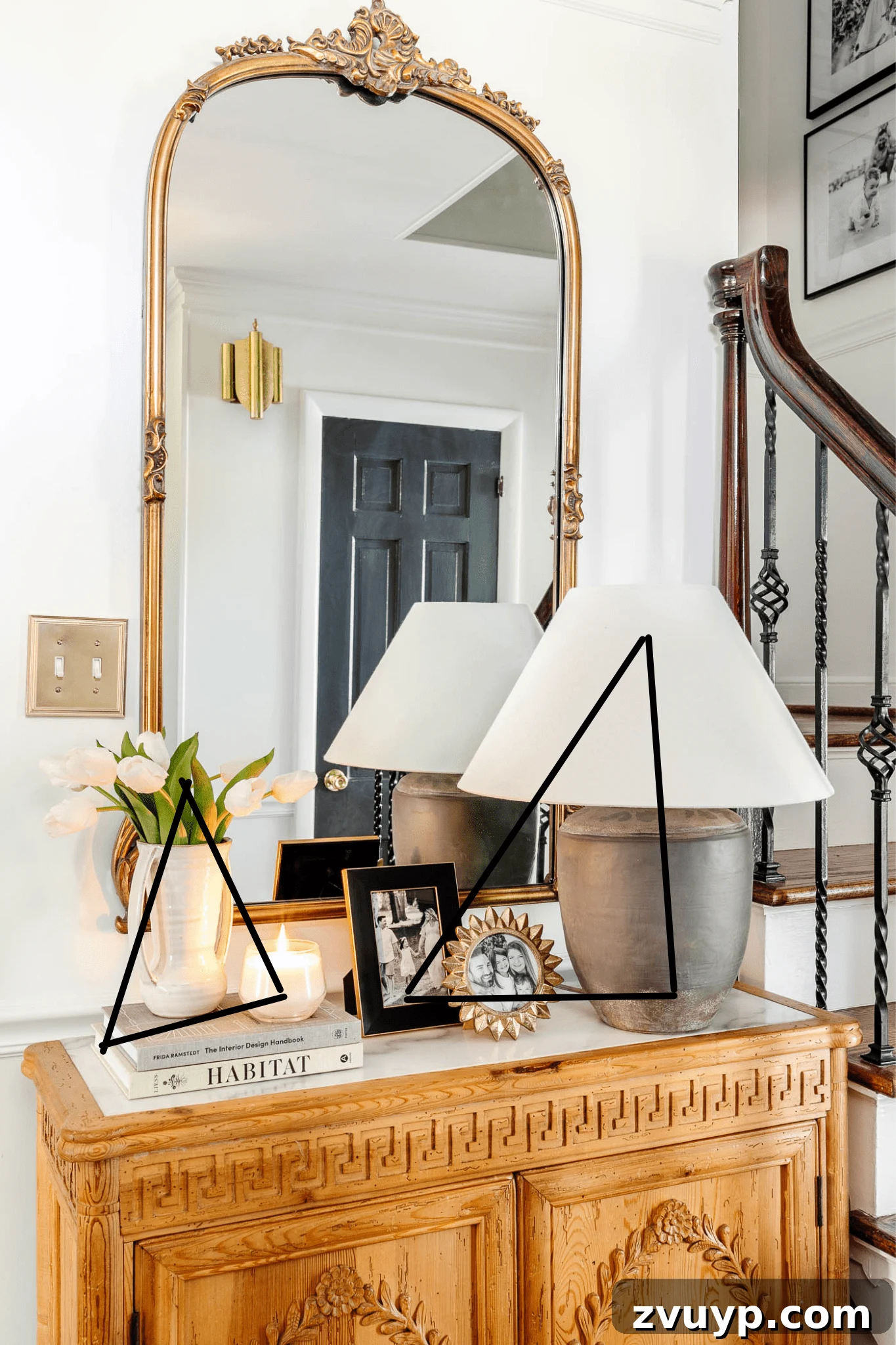 A small entryway decorated with a large gold mirror, a concrete lamp, and a storage chest, demonstrating the impact of fewer, larger decor accents.