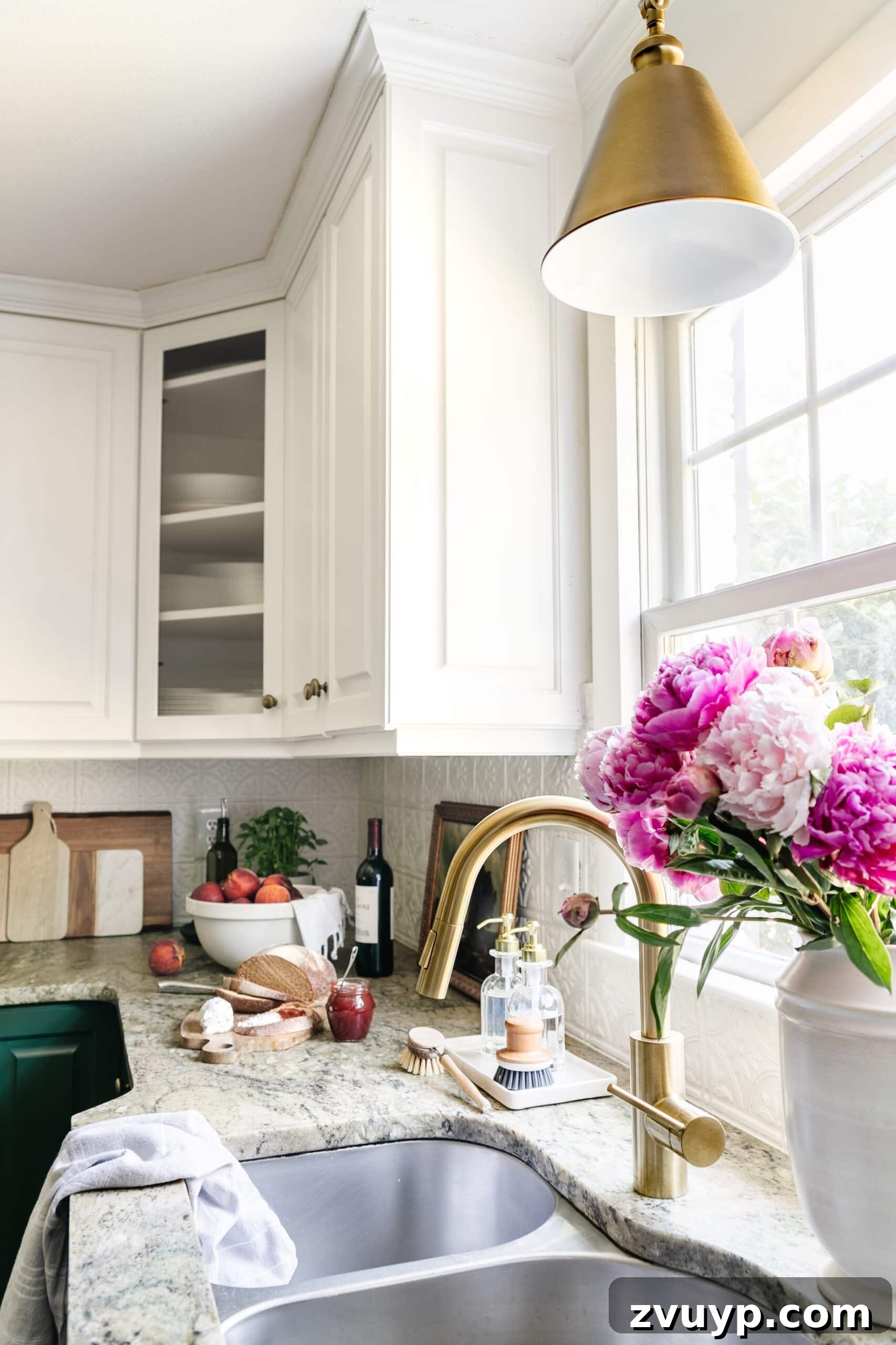 Cozy Cottagecore Kitchen Transformations That Won't Break the Bank 12 A beautifully styled kitchen sink area in front of a window, featuring a new aged brass faucet and a matching brass pendant light, exuding a refreshed charm.