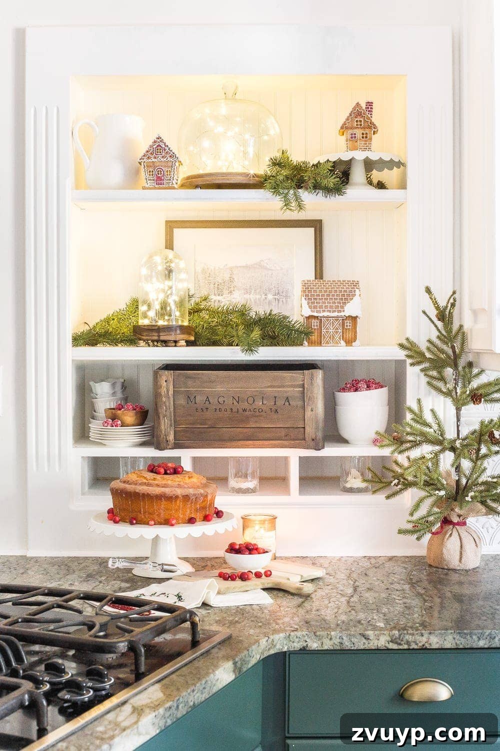 Festive Home Tours 2018 19 A close-up of kitchen shelves adorned with fairy lights under a cake dome and cloche, alongside decorative gingerbread houses.