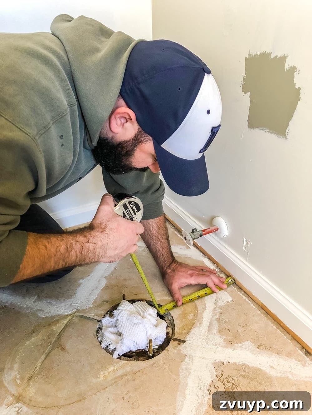DIY Floor Makeover Seamless Sheet Vinyl Over Tile 11 A person kneeling to measure around an obstacle on the floor, specifically a toilet flange, for a precise vinyl flooring template.