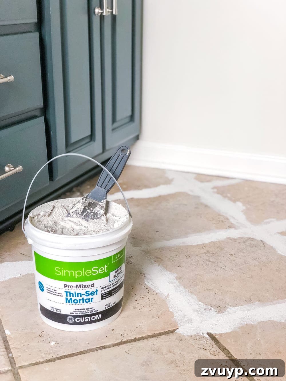 DIY Floor Makeover Seamless Sheet Vinyl Over Tile 6 A hand using a putty knife to fill grout lines with thin-set mortar on a ceramic tile floor.