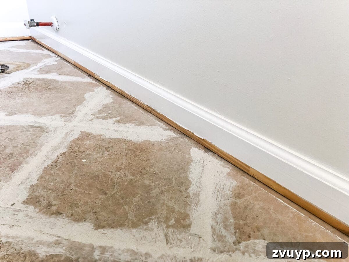 DIY Floor Makeover Seamless Sheet Vinyl Over Tile 9 A pry bar being used to carefully remove shoe molding from a baseboard, preparing the room for flooring installation.