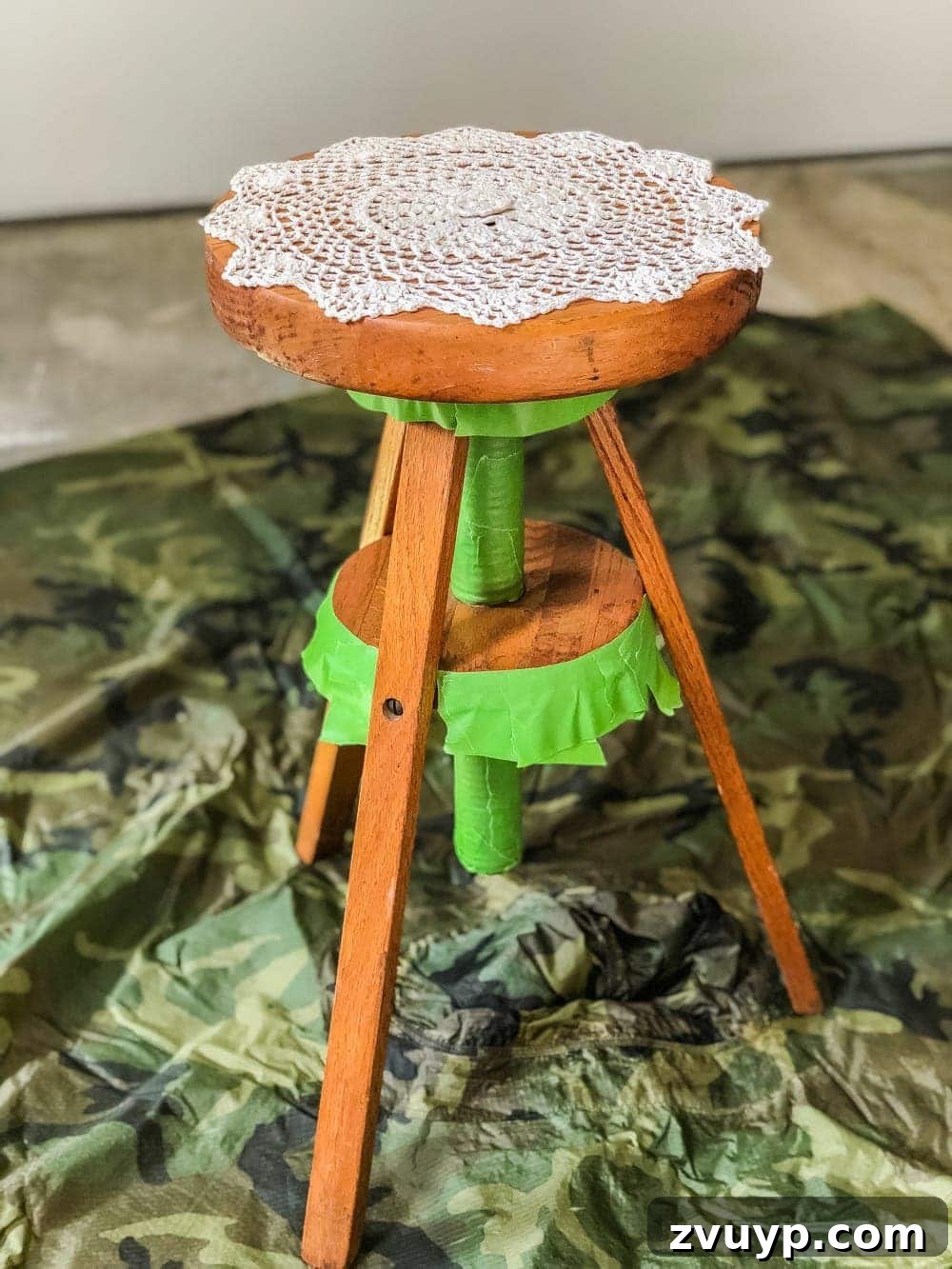 Closeup of a doily placed on top of a piano stool, ready for spray priming and painting to create a delicate stencil pattern for a designer-inspired DIY plant stand.