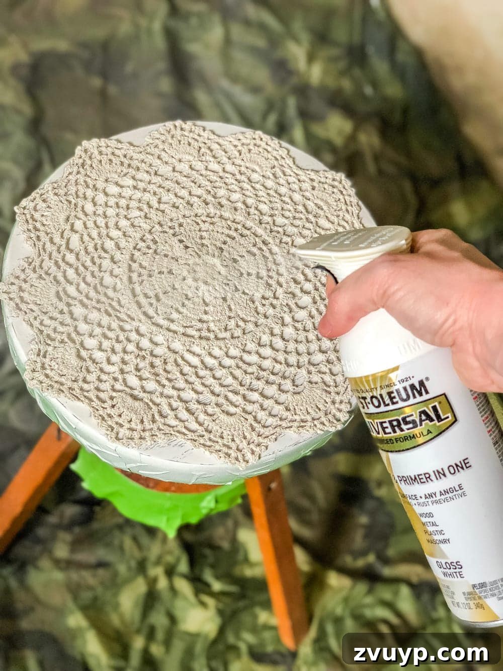 The finished DIY plant stand, transformed from a piano stool with white spray paint and a delicate doily stencil, ready to enhance any home decor with its global-inspired style.