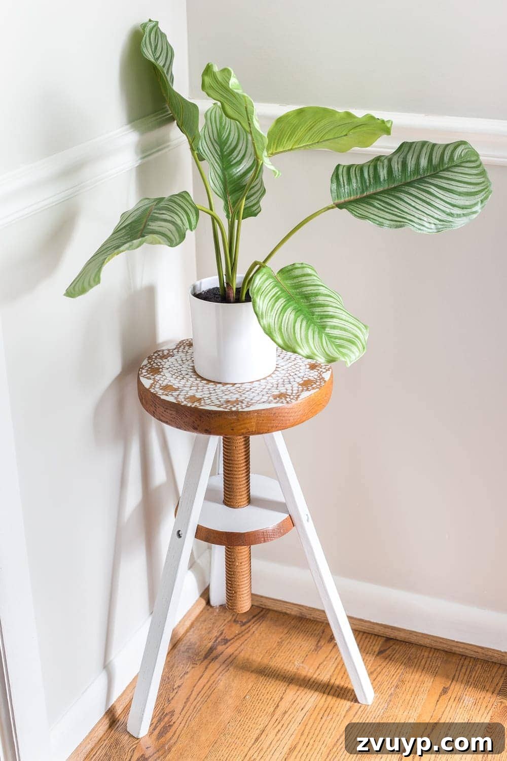 A close-up view of the doily stenciled piano stool plant stand, showcasing its intricate detail and how it complements the surrounding global-inspired home decor in a cozy hallway nook.