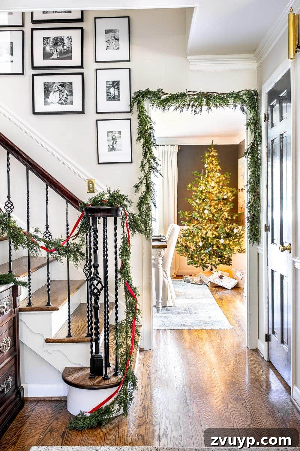 Festive Home Tour 6 Christmas decor ideas: A traditional foyer with realistic faux garland, framed 'O Holy Night' sheet music, and black-and-white family photos on a staircase. Blends modern elegance with sentimental details.