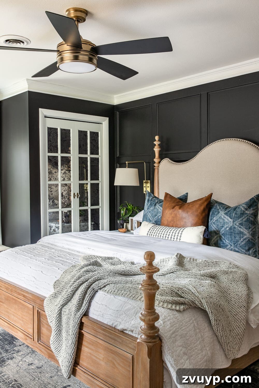 A Masterpiece in Mood: Our Modern Vintage Master Bedroom Unveiled 7 Moody modern vintage master bedroom featuring a cozy bed with layered textiles, including an indigo mud cloth pillow and a textured bedspread, against black walls.