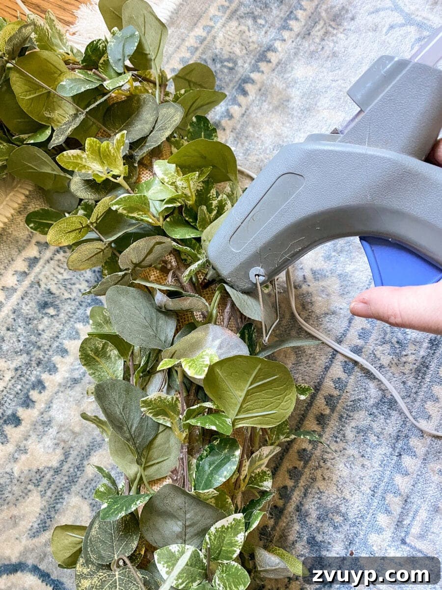 Transforming a Pool Noodle into a Unique Wreath 10 Attaching greenery to the fabric wreath form with hot glue