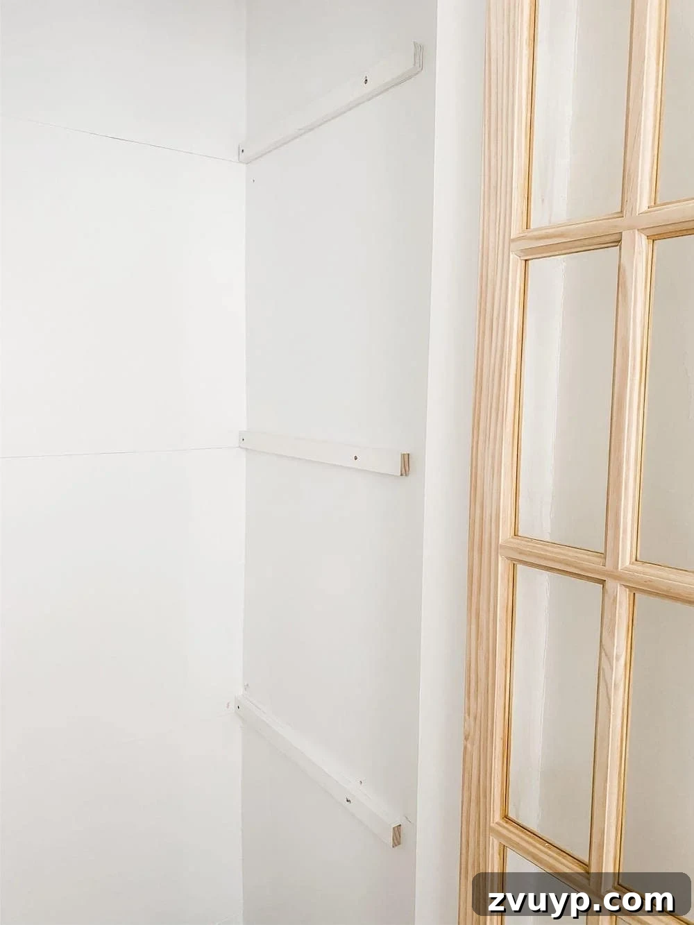 Close-up of a 1x2 wooden brace being screwed into a wall stud inside a closet