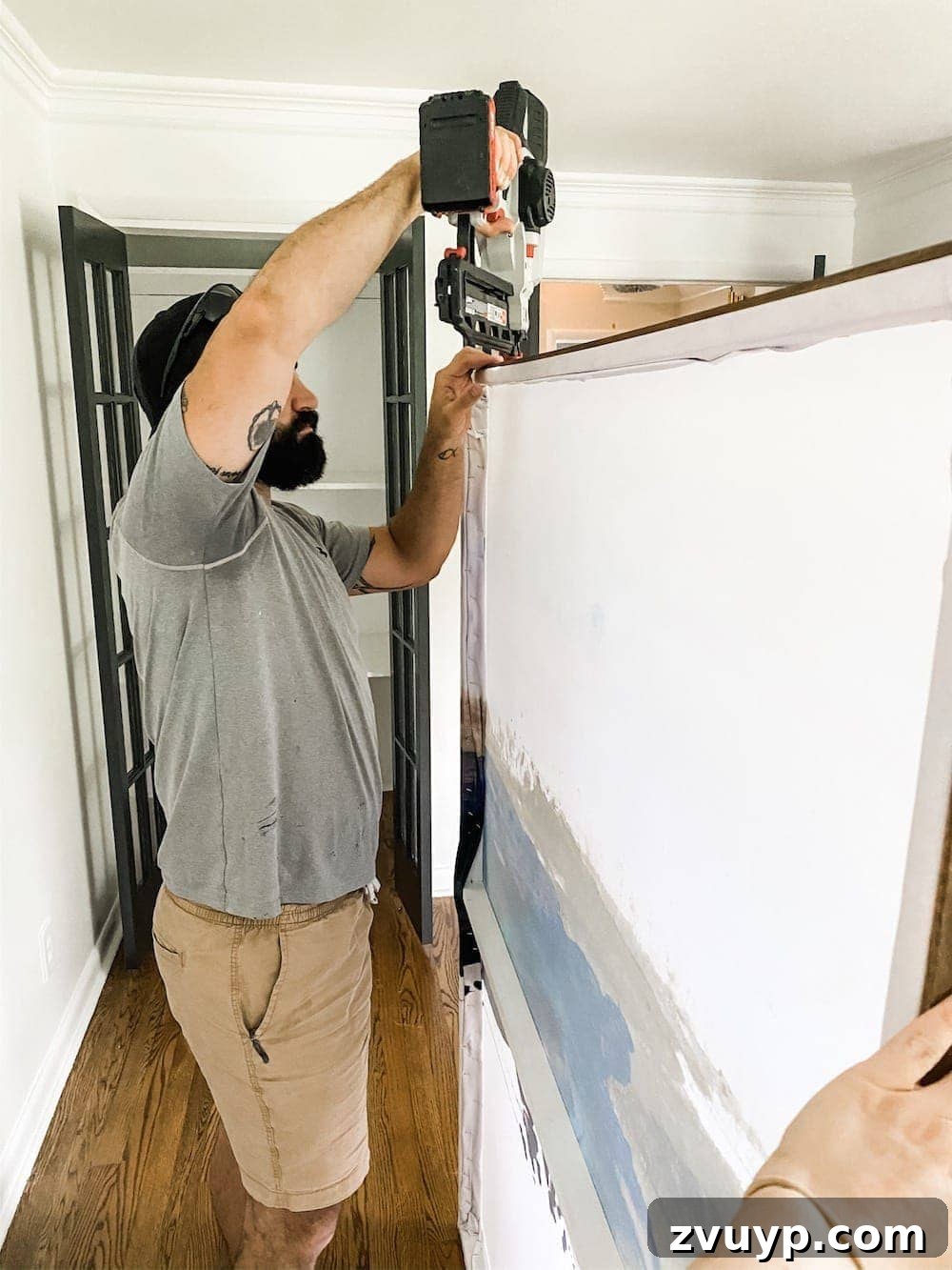 Transform a Shower Curtain into Statement Wall Art 12 Brad nail gun being used to attach a stained lattice strip to the top edge of the DIY wall art.