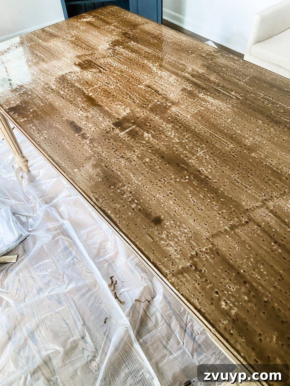 DIY Furniture Evolution: From Raw Wood to Custom Workspaces 5 Close-up shot of an unfinished table being stained with a brush, showing the process of applying wood stain.