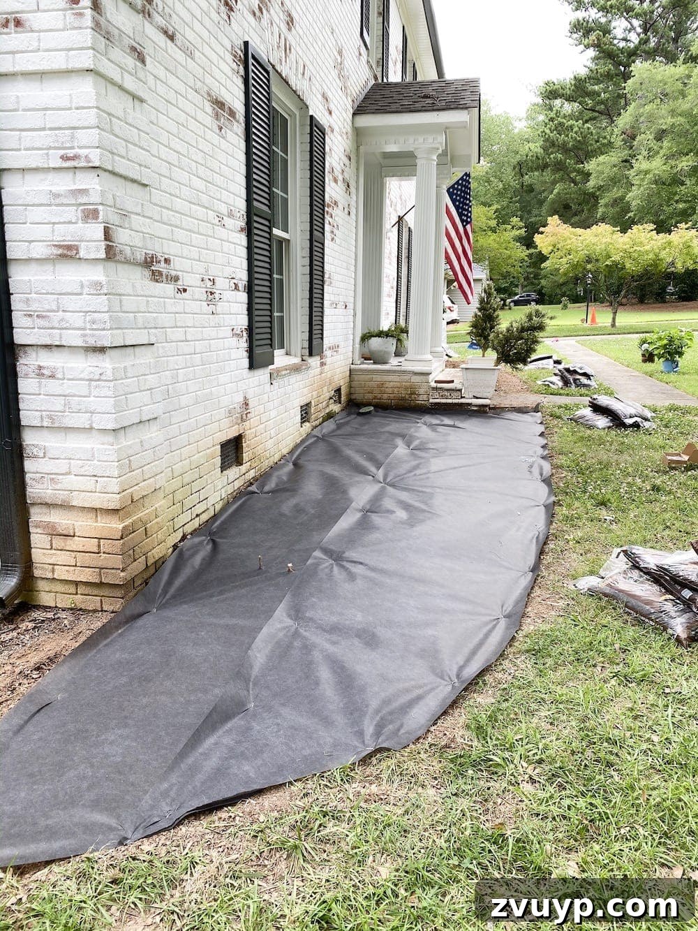 Front Flower Bed DIY Transformation 13 Installing black landscape fabric over a tilled flower bed, securing it with garden staples for weed control.