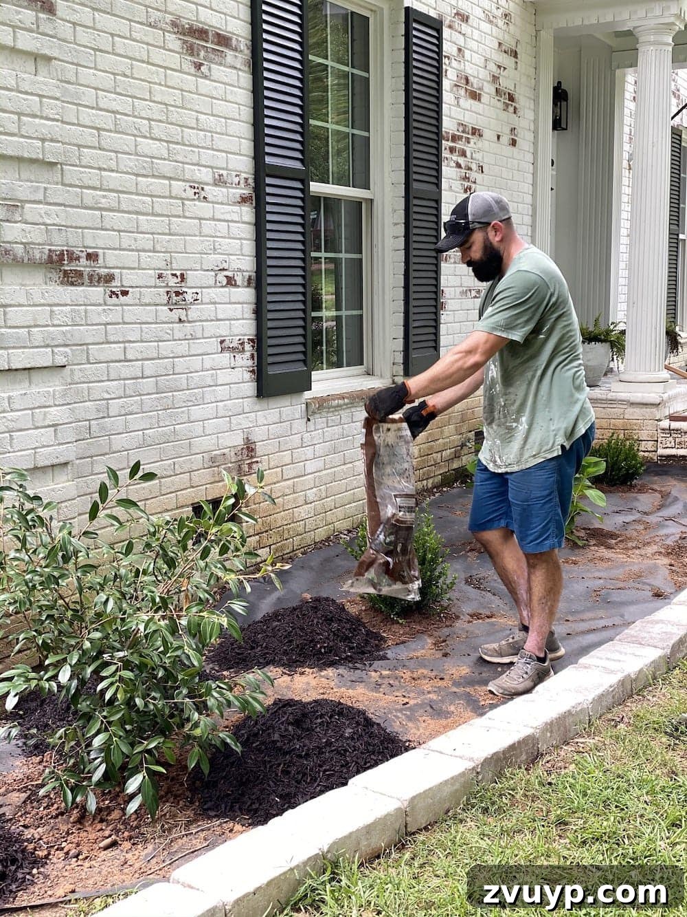 Front Flower Bed DIY Transformation 16 Applying brown rubber mulch over the landscape fabric and around the new plants in the flower bed.