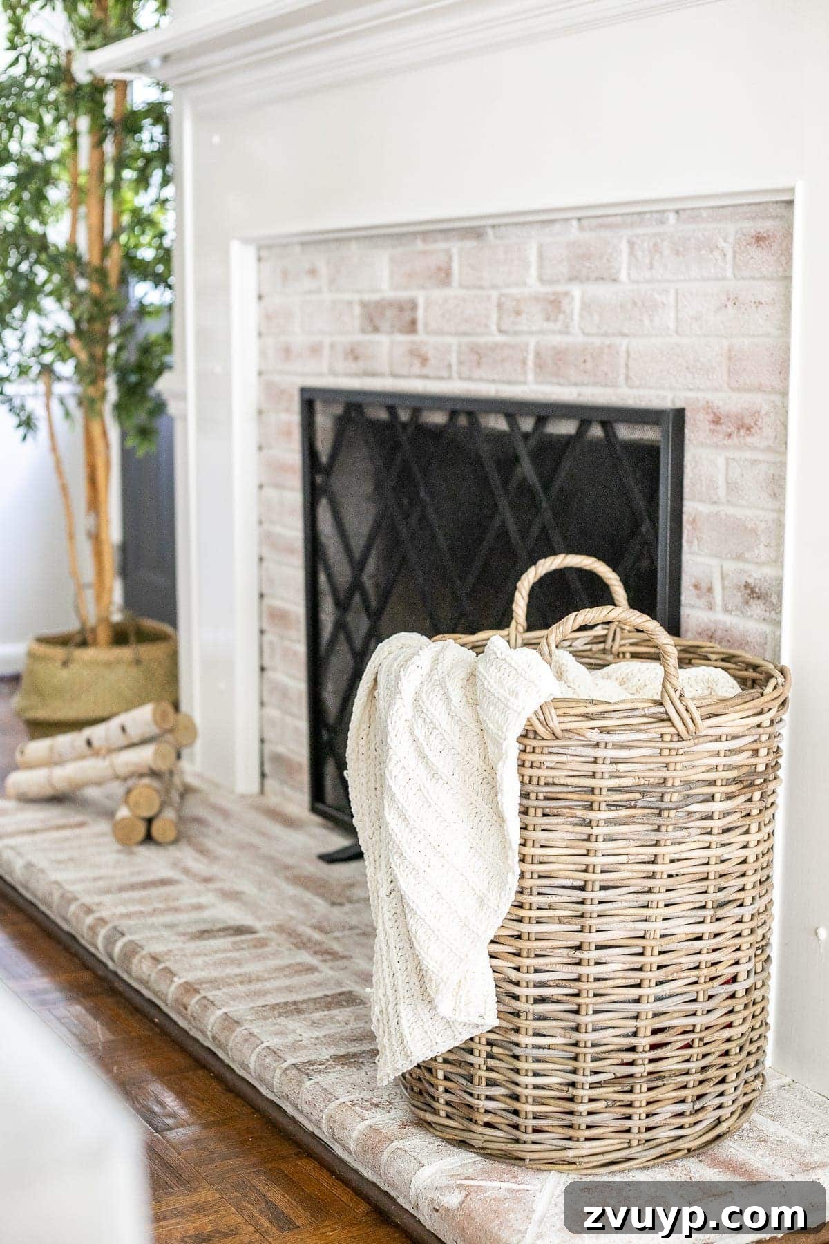 An Earthy Fall Living Room and My Go-To Budget Fall Decor Capsule 9 A charming woven basket filled with a cable knit throw blanket, placed beside a limewashed brick fireplace, creating a rustic and cozy corner.