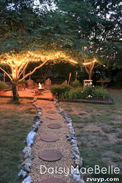 Elevate Your Outdoor Space: 15 Stunning Fire Pit Designs 12 Charming fire pit area illuminated by warm string lights suspended gracefully in the surrounding trees.