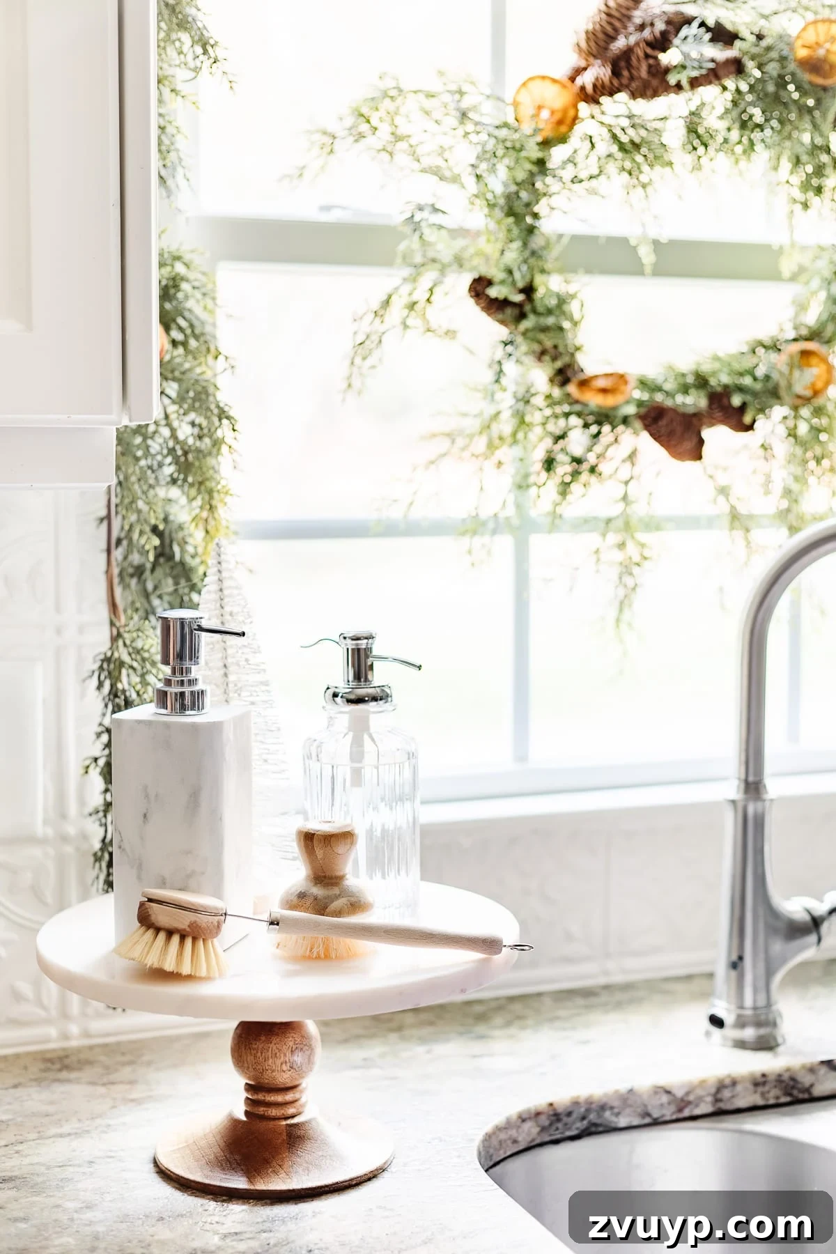 cake stand next to kitchen sink with soaps and a bottle brush tree