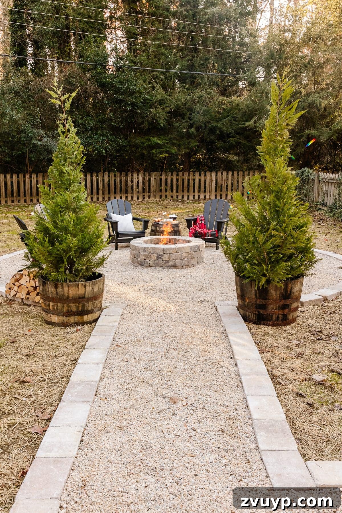 Weekend Wonder: DIY Pea Gravel Fire Pit 23 Backyard fire pit with pea gravel, stone edging, and black Adirondack chairs, enhanced with potted evergreens.