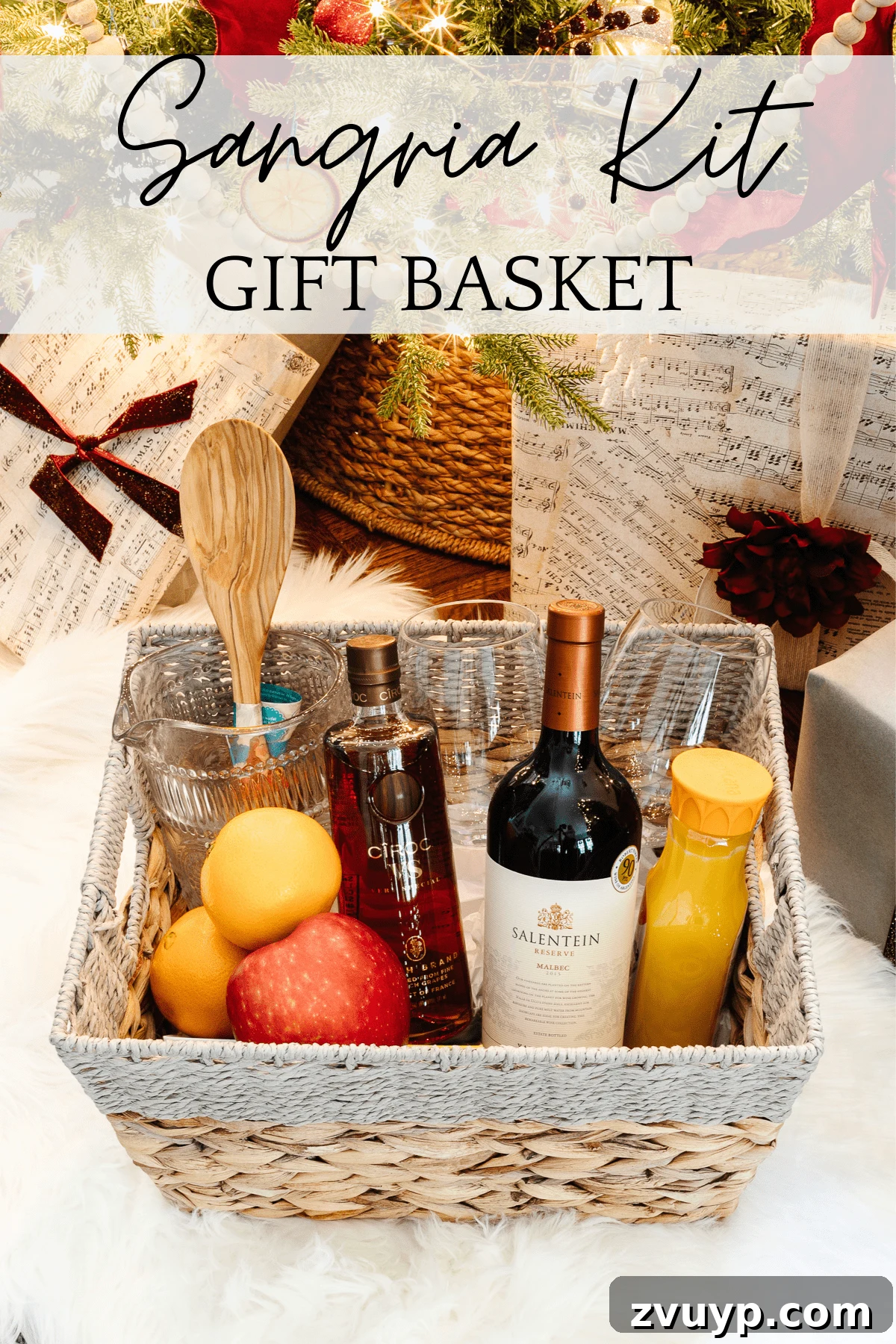 50 Festive Hamper Inspirations 9 Sangria Kit Gift Basket with a pitcher, wine glasses, wooden spoon, red wine, brandy, orange juice, brown sugar, oranges, and apples.