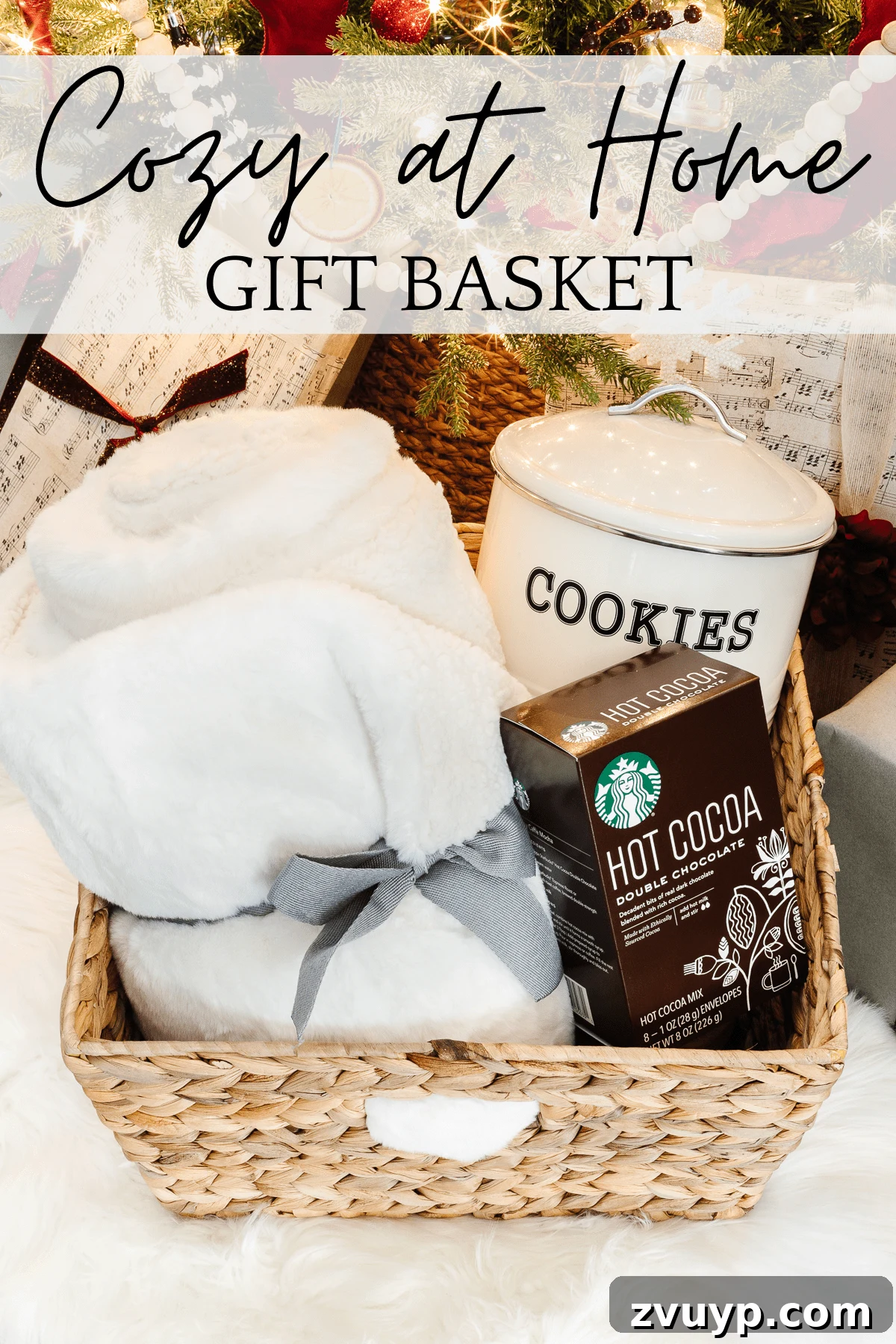 50 Festive Hamper Inspirations 10 Cozy Home Gift Basket with a faux fur throw blanket, candle, picture frame, cookie canister with cookies, and hot cocoa mix.