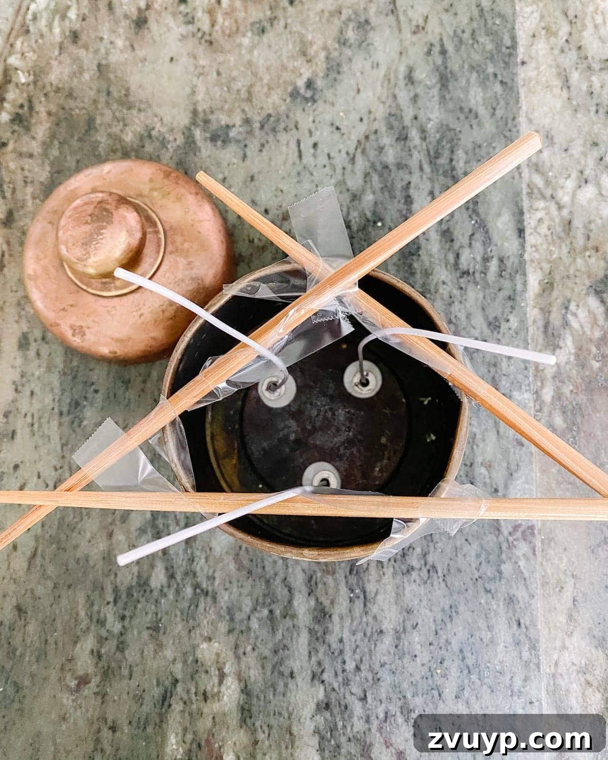 Transforming Thrifted Brass into Elegant Candles 7 A wick held upright by chopsticks in a vintage canister, illustrating the setup for DIY candle making.