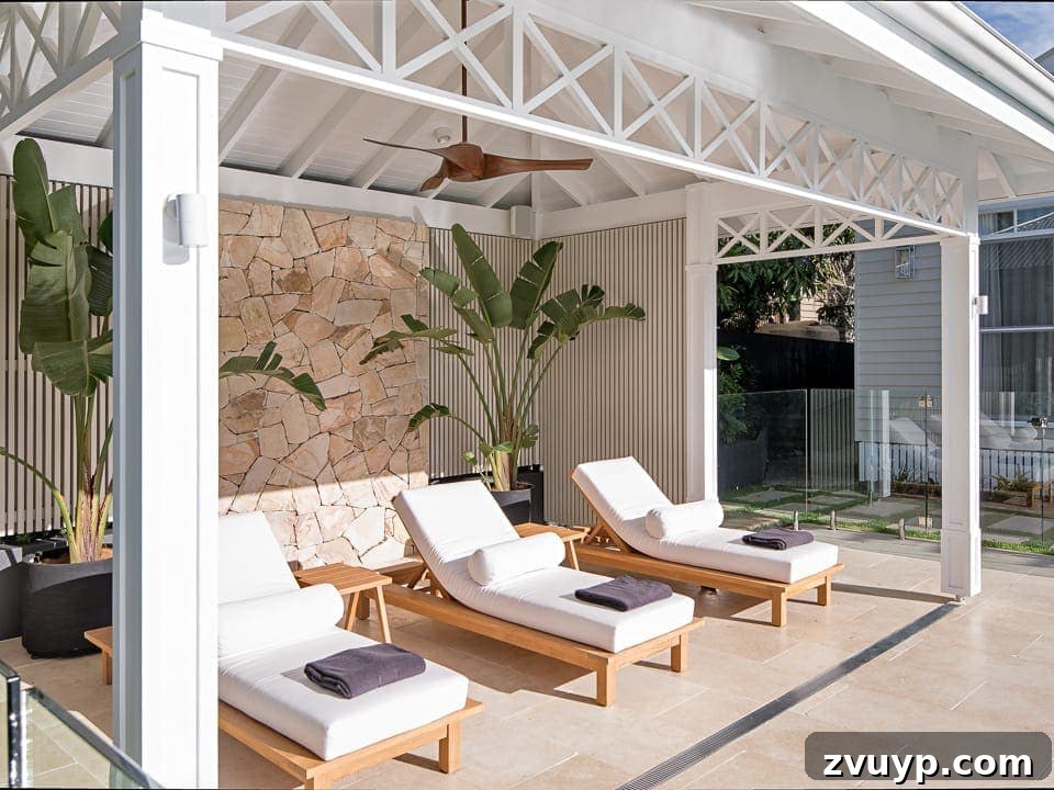7 Pool Cabana Ideas for Your Backyard Oasis 3 Elegant white cabana featuring comfortable outdoor chaise lounge chairs and a textured stone wall backdrop.