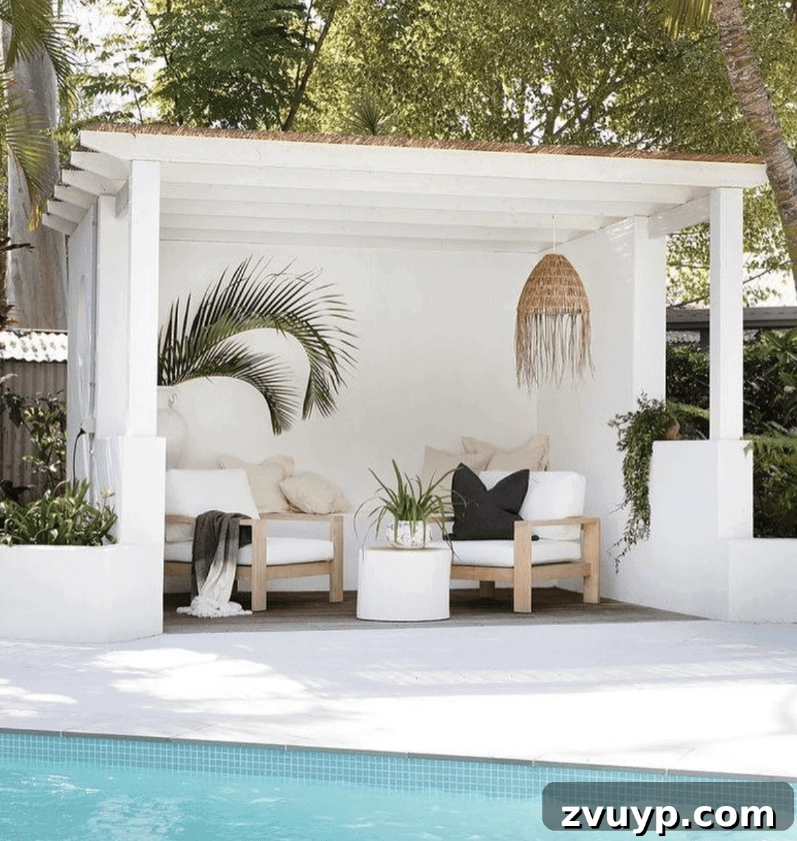 7 Pool Cabana Ideas for Your Backyard Oasis 4 Lush tropical plants and a stylish rattan pendant light illuminate a bright white pool cabana, creating an inviting natural ambiance.