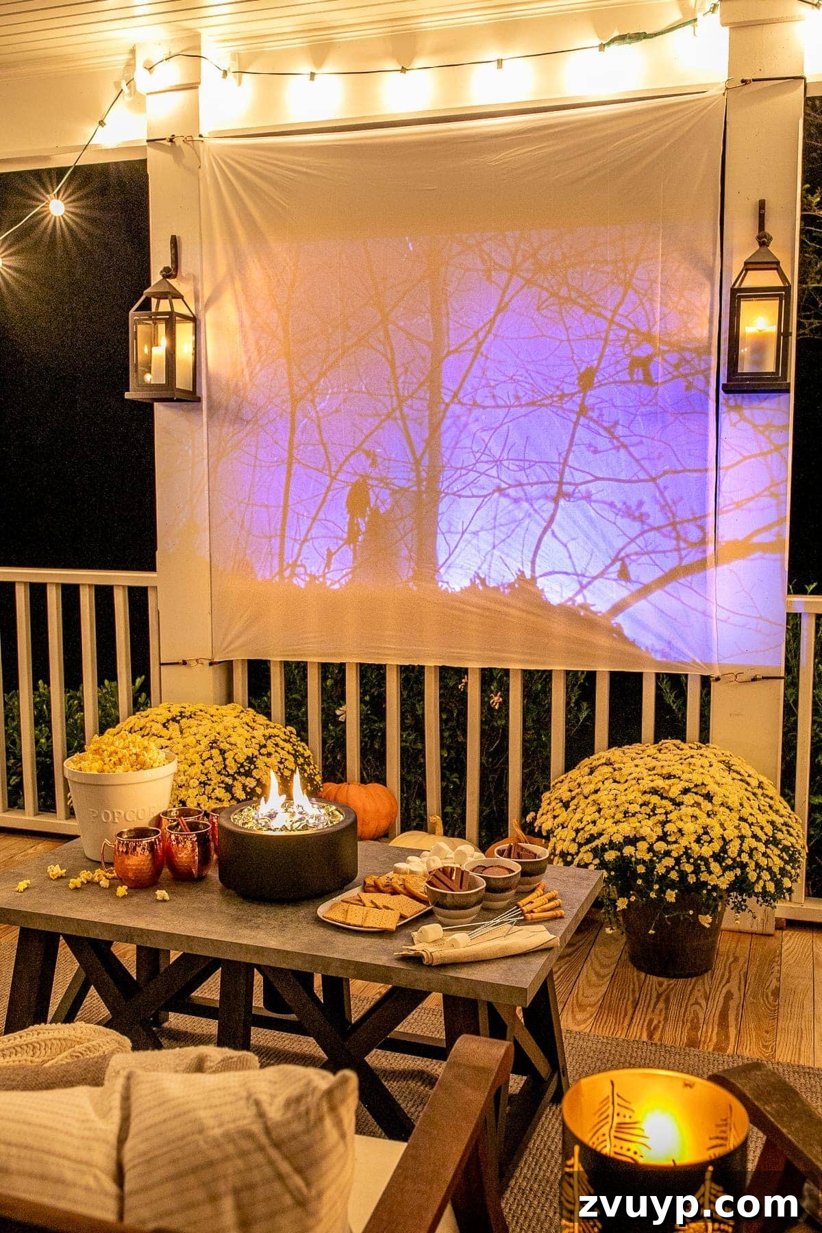 Create an Epic Backyard Movie Night Without Breaking the Bank 17 fall movie playing on an outdoor movie screen on a back porch decorated for fall with pumpkins, mums, and tabletop fire pit