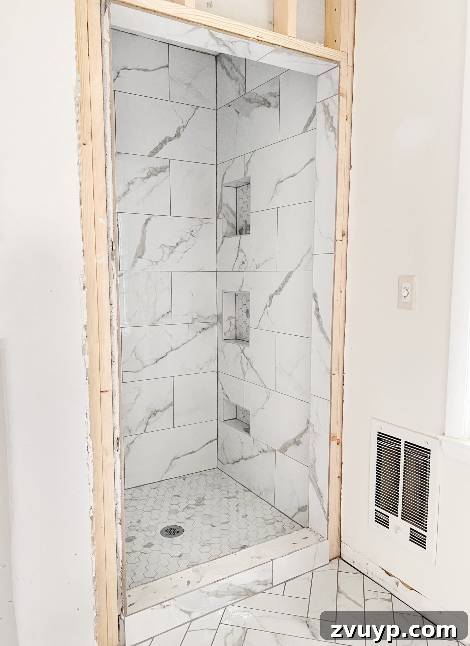 Faux Marble Herringbone: Our Shower Transformation Unfolds 9 A beautifully renovated shower featuring large format faux marble tiles on the walls and a hexagon tile floor, complemented by gray grout.