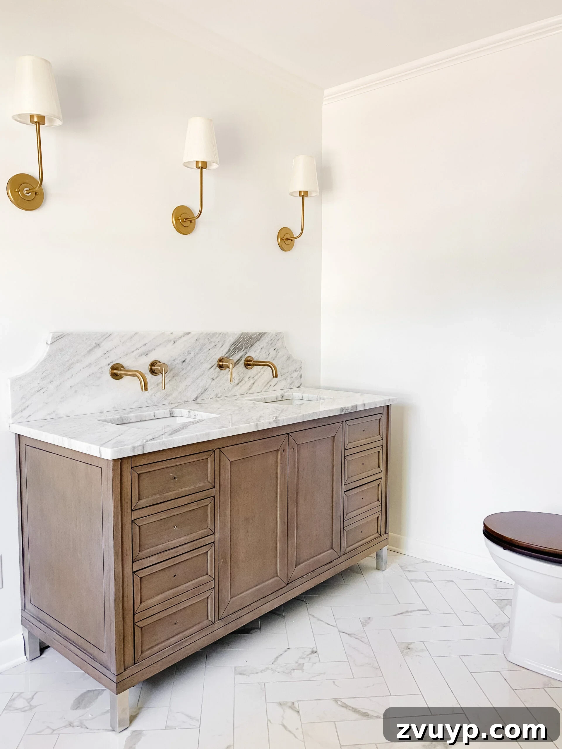 Our En Suite Bathroom Remodel: Faucets Are Finally In! 2 scalloped marble backsplash with gold wall mount faucets, faux marble porcelain tile herringbone floor, and wooden vanity in en suite bathroom