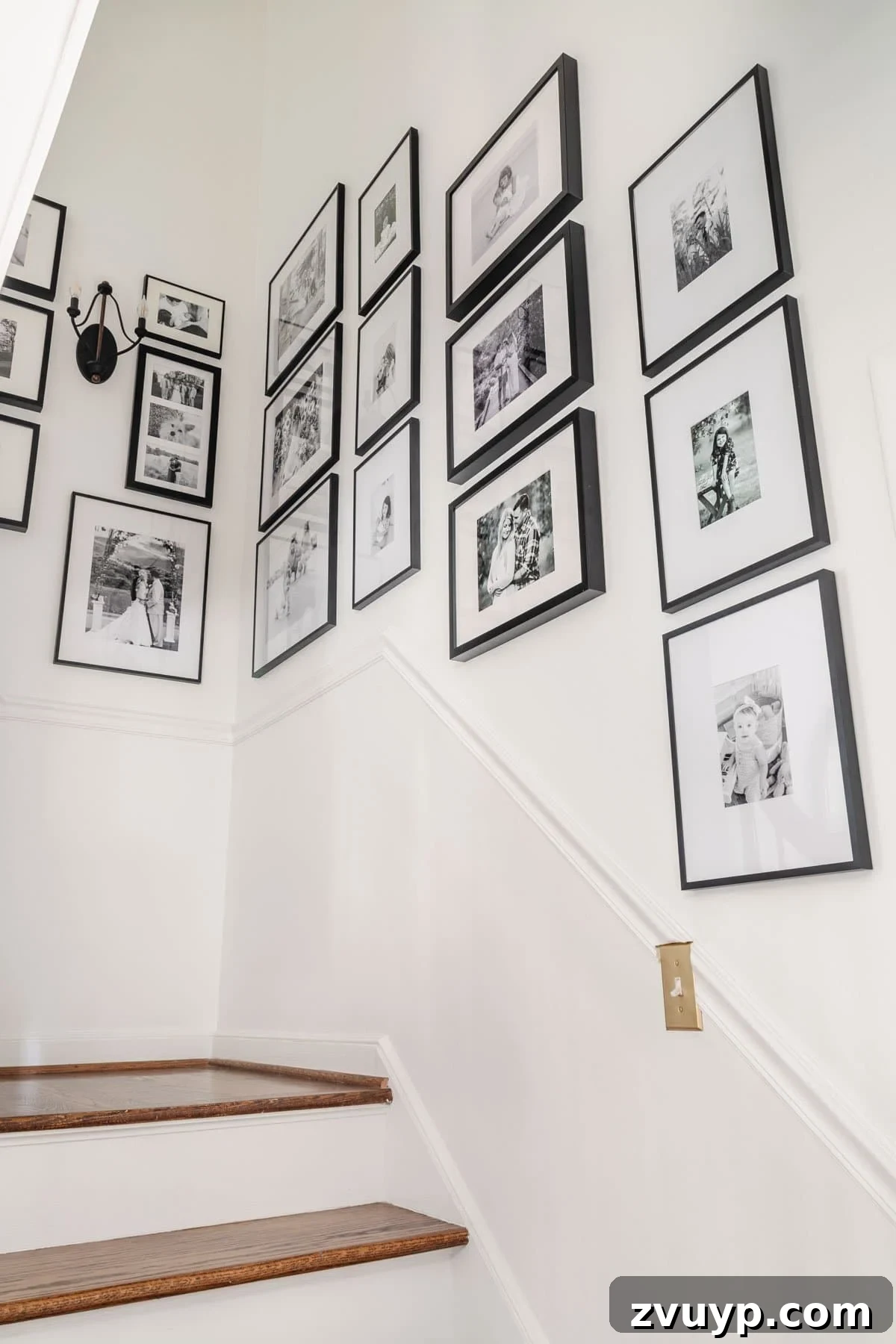 Vintage Meets Modern Foyer Makeover 14 Elegant black and white staircase gallery wall showcasing a diverse collection of framed family photographs, creating a striking and personalized visual narrative along the stairs.