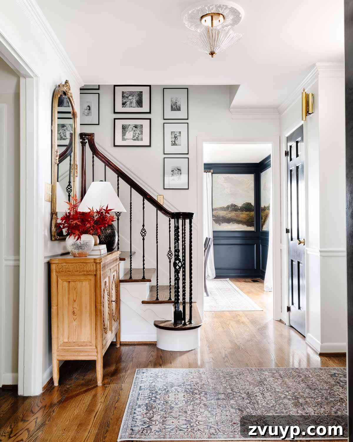Vintage Meets Modern Foyer Makeover 4 Cozy autumn-themed foyer with a stylish entryway table adorned with a vase of fall leaves, a classic mirror, and a warm lamp, complemented by a stairway gallery wall.