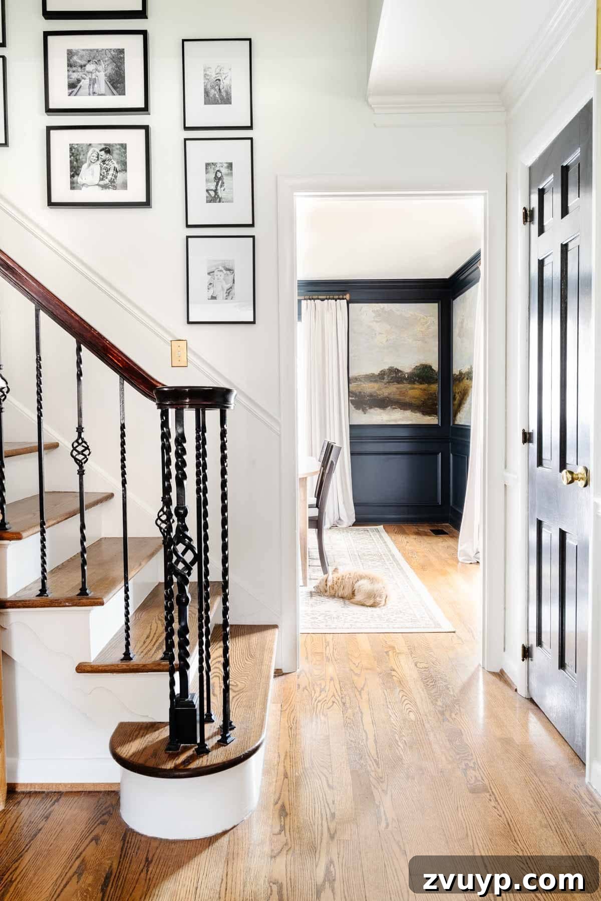 Vintage Meets Modern Foyer Makeover 7 Elegant stairway gallery wall with black frames and family photos, offering a clear view into a dining room adorned with captivating mural wallpaper, exemplifying a blend of old and new decor.