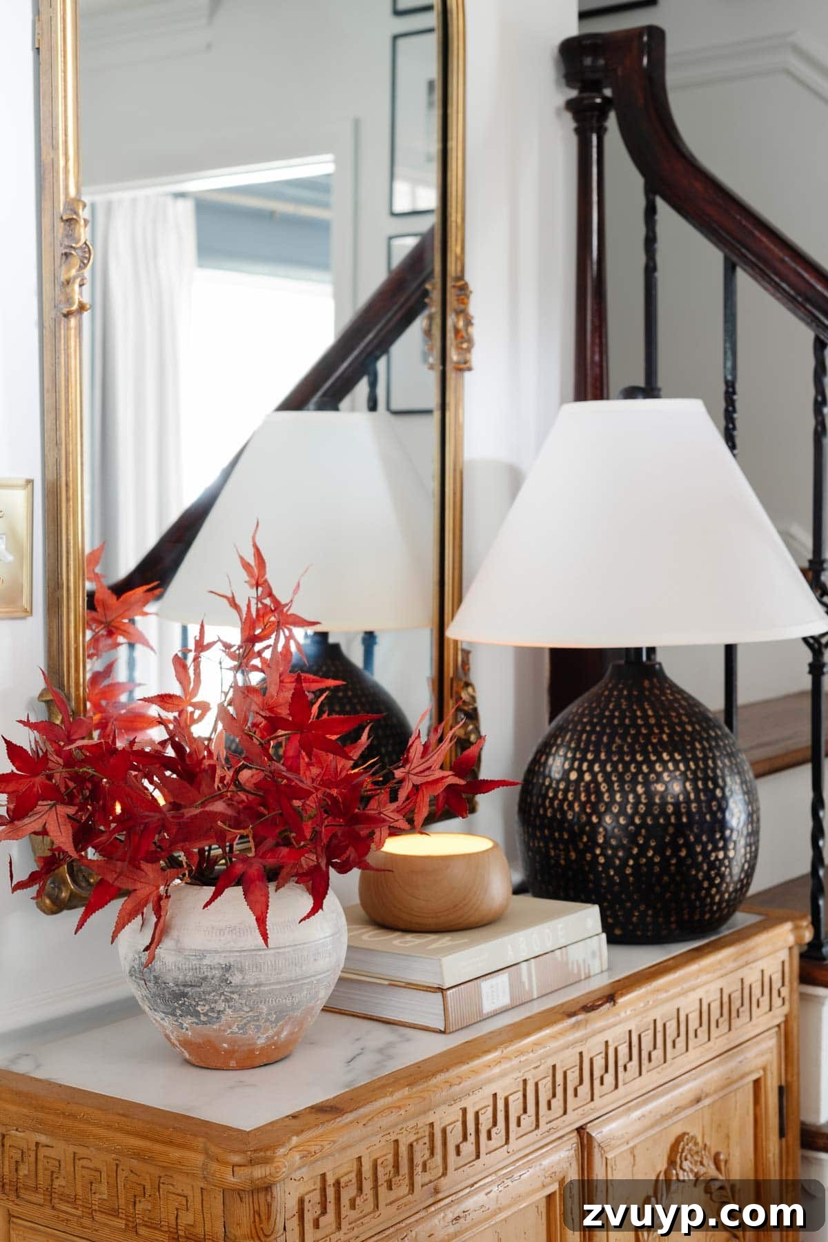 Vintage Meets Modern Foyer Makeover 9 Close-up of a marble-top entryway table adorned with a stylish lamp, a classical mirror, and a beautiful vase overflowing with radiant fall leaves, highlighting intricate details.