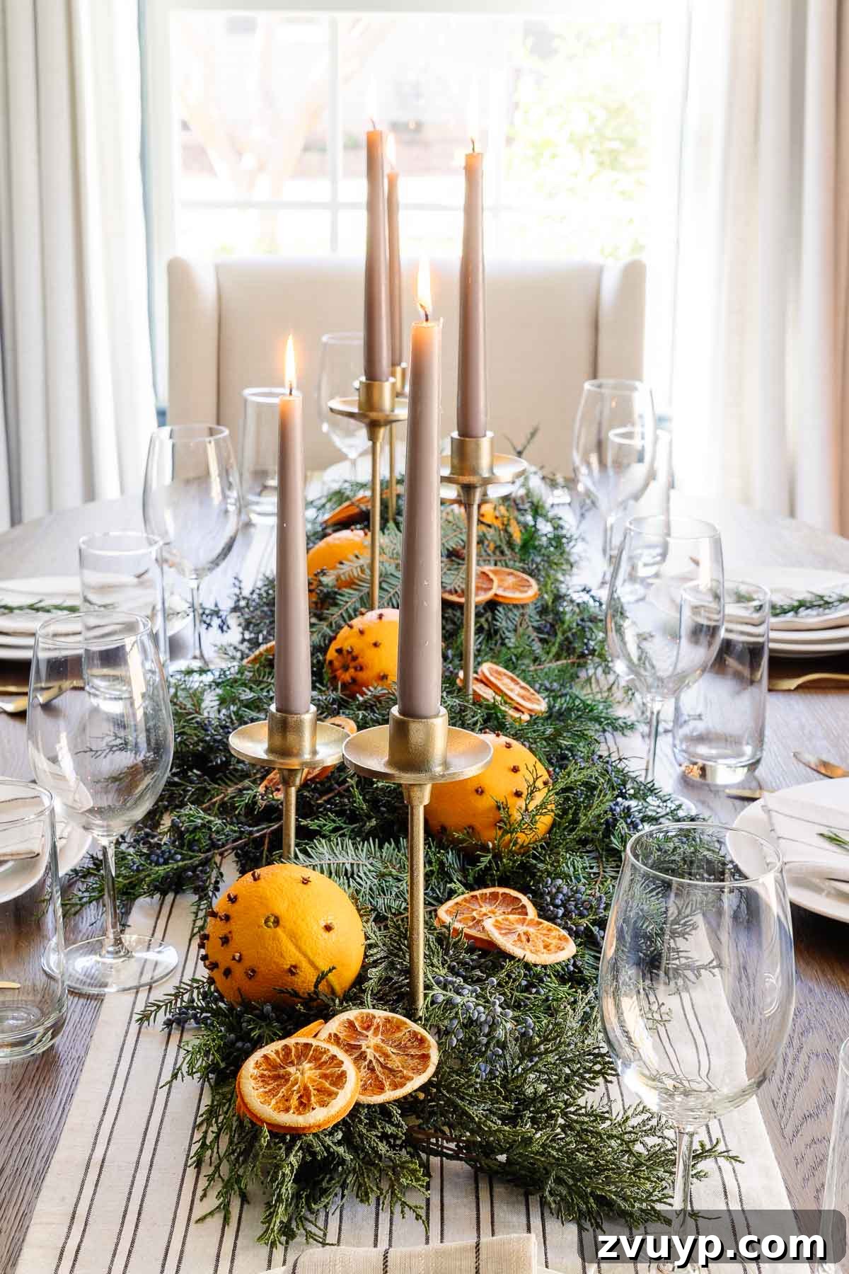 Elegant Christmas Tablescapes for Less 4 Detailed shot of a simple Christmas table centerpiece featuring dried orange slices, fresh evergreen branches, and vibrant juniper berries, embodying a natural, vintage aesthetic