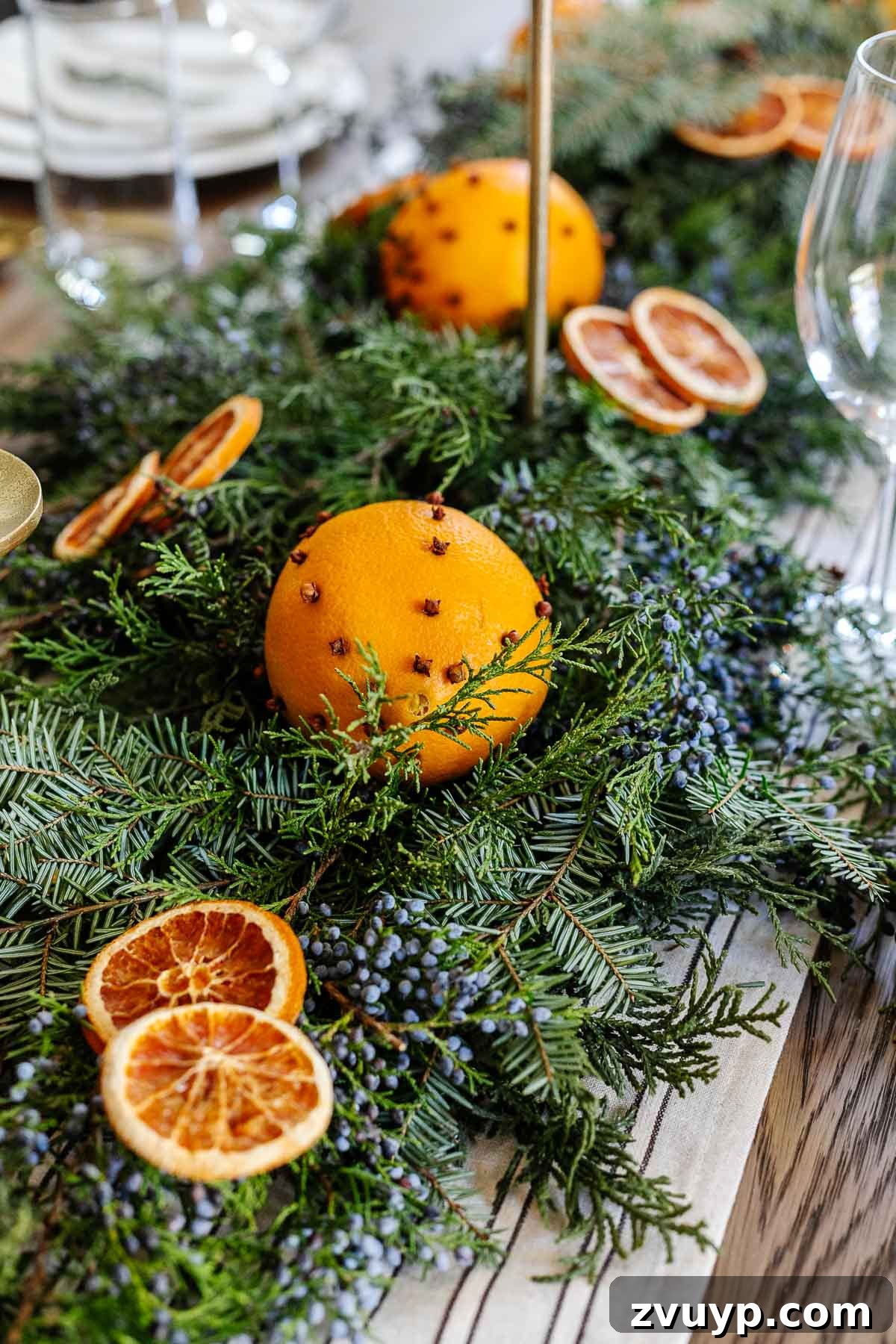 Elegant Christmas Tablescapes for Less 5 Juniper, orange, and evergreen Christmas greenery arranged casually around candle holders, creating a natural and inviting festive atmosphere