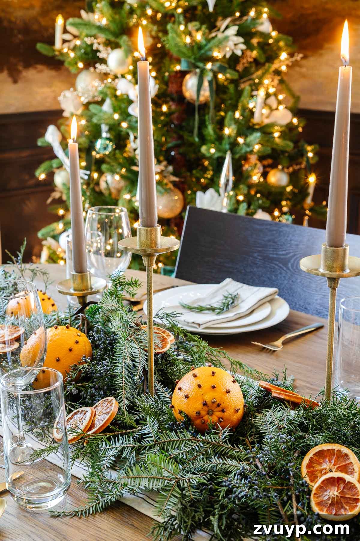 Elegant Christmas Tablescapes for Less 6 Close-up of a rustic Christmas table centerpiece featuring dried orange slices, fresh evergreen sprigs, and scattered juniper berries for a natural touch