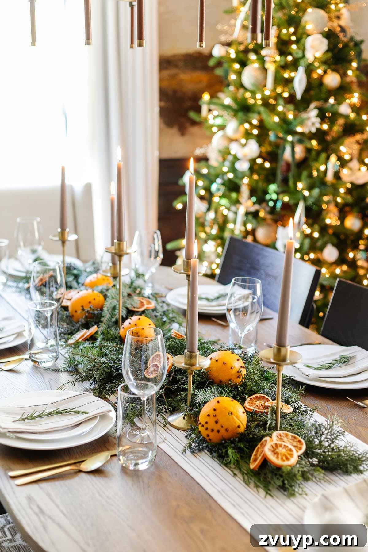 Elegant Christmas Tablescapes for Less 8 A beautifully arranged simple Christmas table centerpiece showcasing dried orange slices, handmade orange pomanders, elegant gold candle holders, and fresh evergreen branches for a natural holiday look