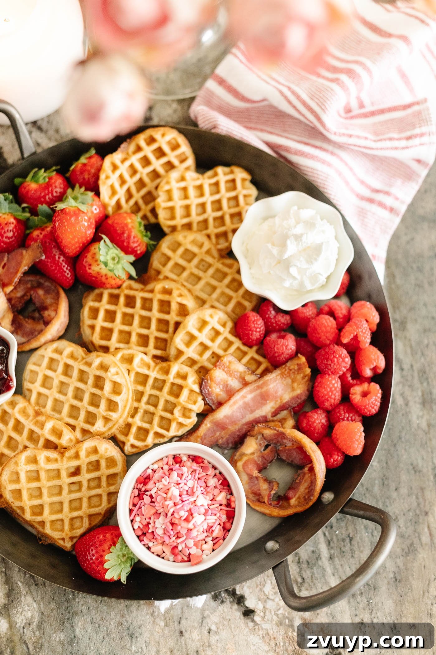A Lover's Morning Board 6 Valentine's Day breakfast charcuterie board with heart shaped waffles, XO bacon, berries, and condiments on a tray